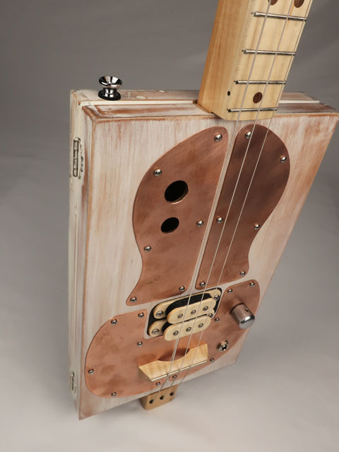 Cigar Box Guitar tilted view with copper pick guard and humbucker pickup. Made by Mike Snowden.
