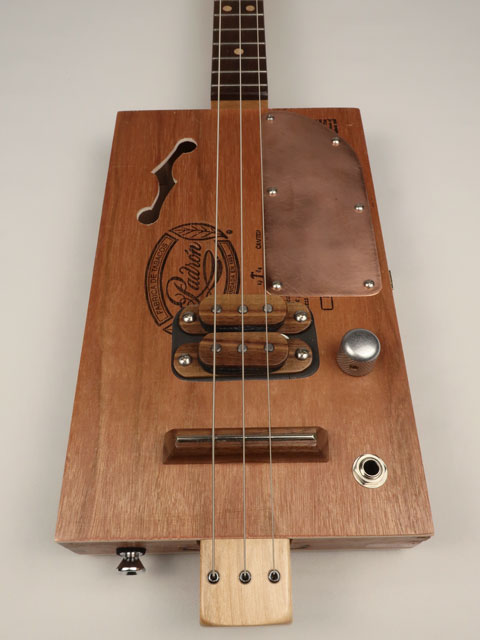 Front view cigar box guitar with copper pick guard and humbucker pickup. 3 string cigar box guitar is made by Mike Snowden.