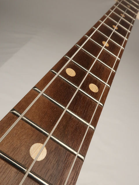 Close-up of a cigar box guitar fretboard with fret markers on a neutral background. The fretboard is walnut and the inlay is maple wood.