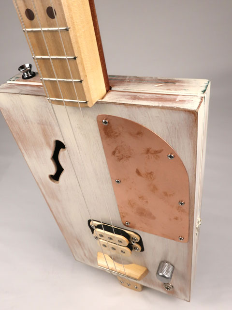 Front tilted view of a 3 string cigar box guitar made with a humbucker pickup and copper pick guard. This cigar box guitar is handmade by Mike Snowden of Snowden Guitars.