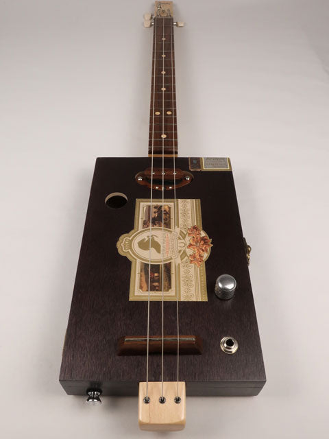 Front view of a 3 string cigar box guitar made with a Pura Raza cigar box. This cigar box guitar is made with walnut and maple with a single coil pickup by Mike Snowden of Snowden Guitars.