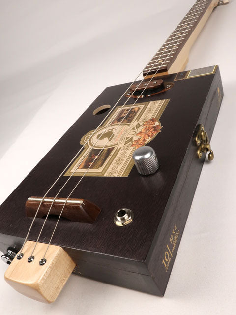 Front tilted view of a 3 string cigar box guitar made with a Pura Raza cigar box. This cigar box guitar is made with walnut and maple with a single coil pickup by Mike Snowden of Snowden Guitars.