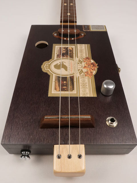 Front view of a 3 string cigar box guitar made with a Pura Raza cigar box. This cigar box guitar is made with walnut and maple with a single coil pickup by Mike Snowden of Snowden Guitars.
