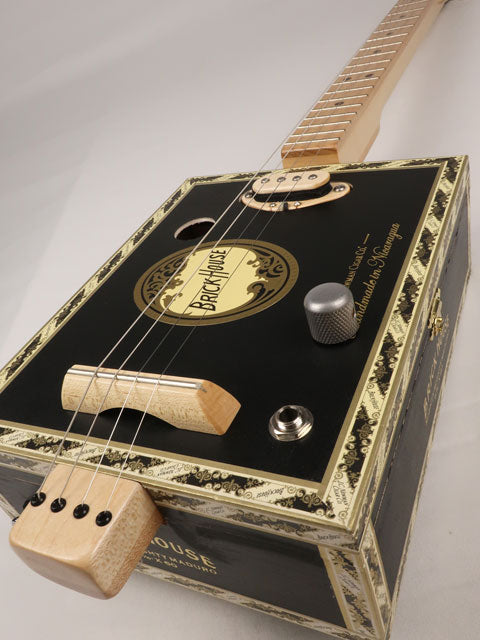 Front tilted view of a 4 string cigar box guitar made with a Brick House cigar box. This cigar box guitar is made with a maple single coil pickup handmade Mike Snowden of Snowden Guitars.