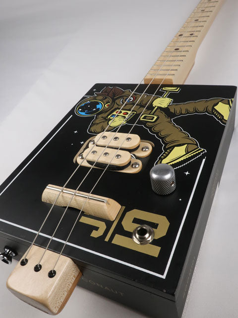 Front view of a 3 string cigar box guitar with an astronaut space suit on the front. Maple neck and maple humbucker pickup handmade by Mike Snowden of Snowden Guitars.