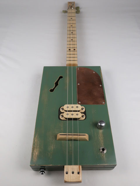 Front view of a 3 string cigar box guitar with a maple humbucker pickup and copper pick guard. This cigar box guitar as a maple neck and was handmade by Mike Snowden of Snowden Guitars.