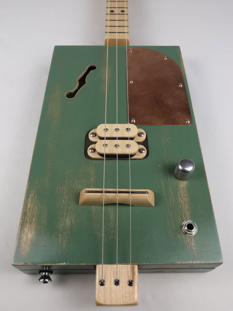 Front view of a 3 string cigar box guitar with a maple humbucker pickup and copper pick guard. This cigar box guitar as a maple neck and was handmade by Mike Snowden of Snowden Guitars.