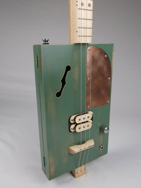 Tiled front view of a 3 string cigar box guitar with a maple humbucker pickup and copper pick guard. This cigar box guitar as a maple neck and was handmade by Mike Snowden of Snowden Guitars.