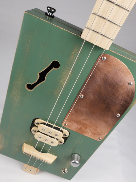 Tilted view of a 3 string cigar box guitar with a maple humbucker pickup and copper pick guard. This cigar box guitar as a maple neck and was handmade by Mike Snowden of Snowden Guitars.