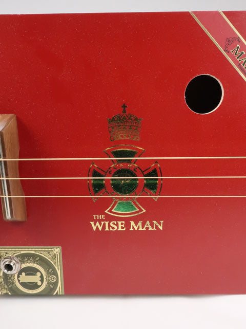 Closeup view of a sound hole on a red cigar box guitar. This cigar box guitar is handmade by Mike Snowden and has a walnut bridge.