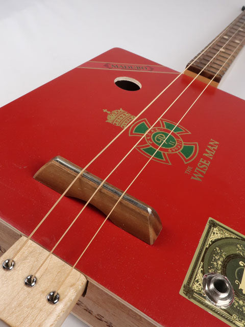 Closeup view of a red cigar box guitar handmade by Mike Snowden. 3 string cigar box guitar with a walnut bridge and sound hole.
