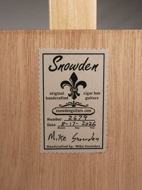 Back view of a cigar box guitar with a Snowden Guitars sticker on the back of the cigar box. The tag shows the date and number of guitars handmade by Mike Snowden.