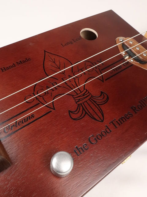 Front tilted view of a 3 string cigar box guitar made with a New Orleans Cigar Factory cigar box handmade by Mike Snowden of Snowden Guitars.