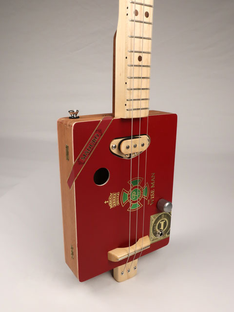 Front tilted view of The Wise Man 3 string cigar box guitar handmade by Mike Snowden. This cigar box is made with a red cigar box with The Wise Man printed on the front.