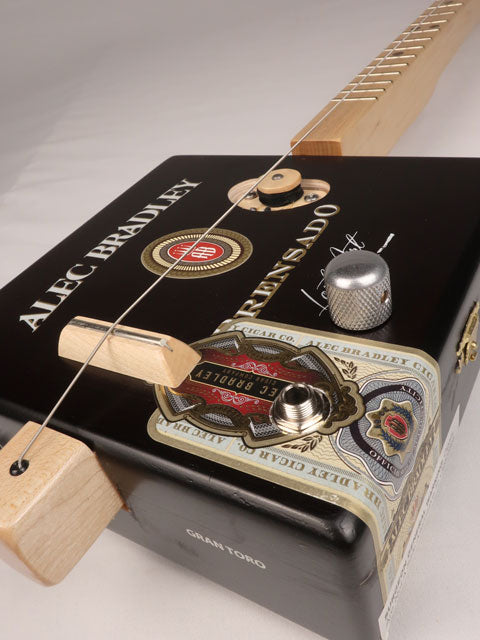 Front tilted view of a one string cigar box guitar made with a Alec Bradley cigar box. Handmade by Mike Snowden of Snowden Guitars. 
