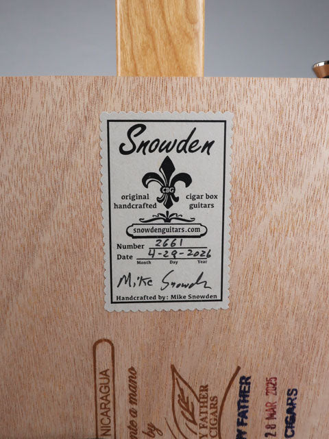 Close-up view of a Snowden Guitars logo on the back of a cigar box guitar. This sticker shows the date and number of guitars Mike Snowden has built.
