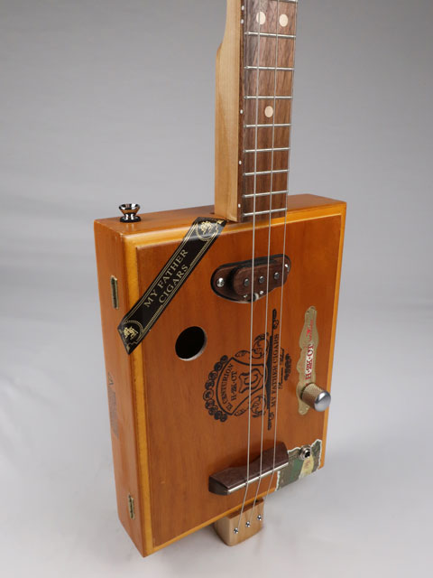 Tilted view of a 3 string Cigar Box Guitar made with a walnut single coil pickup. This cigar box guitar was handmade by Mike Snowden of Snowden Guitars.