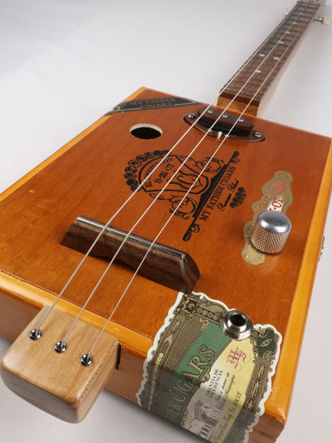 Tilted front view of a 3 string Cigar Box Guitar made with a walnut single coil pickup. This cigar box guitar was handmade by Mike Snowden of Snowden Guitars.