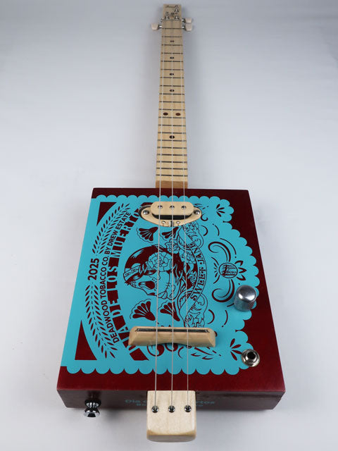Front view of a 3 string cigar box guitar with Sweet Jane logo printed in teal on a red cigar box. This cigar box guitar has a maple neck and maple single coil pickup and is handmade by Mike Snowden of Snowden Guitars.
