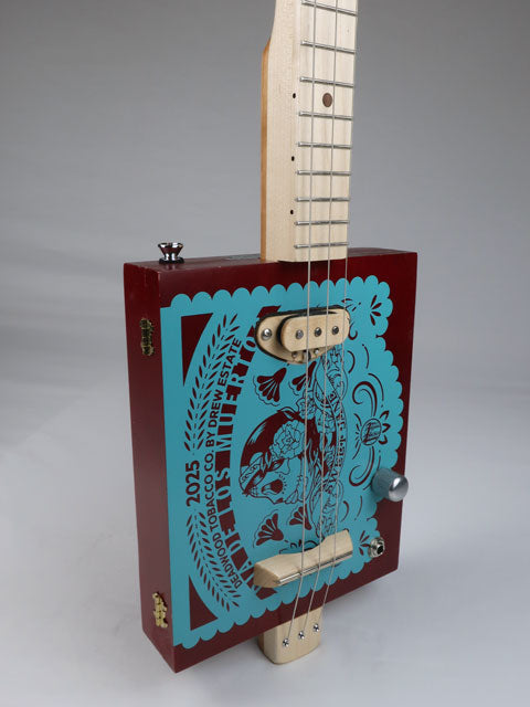 Front angle view of a 3 string cigar box guitar with Sweet Jane logo printed in teal on a red cigar box. This cigar box guitar has a maple neck and maple single coil pickup and is handmade by Mike Snowden of Snowden Guitars.