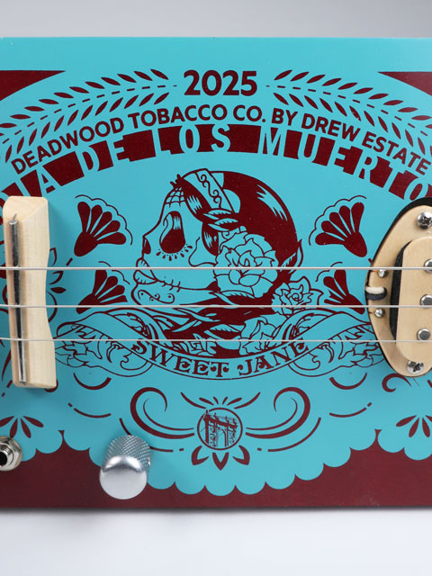Front view of a 3 string cigar box guitar with Sweet Jane logo printed in teal on a red cigar box. This cigar box guitar has a maple neck and maple single coil pickup and is handmade by Mike Snowden of Snowden Guitars.