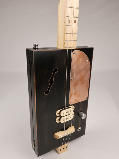 Front tilted view of a 3 string cigar box guitar with a copper pick guard and maple humbucker. This cigar box guitar is handmade by Mike Snowden of Snowden Guitars.