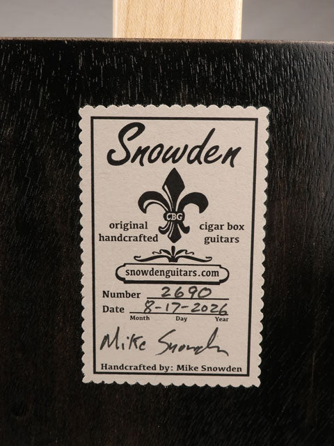 Back view of a cigar box guitar with a Snowden Guitars logo printed on the back. The label shows the date and number of guitars made by Mike Snowden of Snowden Guitars.
