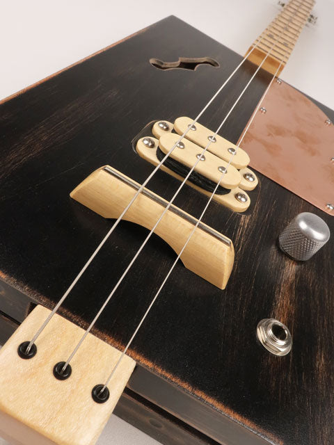 Front tilted view of a 3 string cigar box guitar with a copper pick guard and maple humbucker. This cigar box guitar is handmade by Mike Snowden of Snowden Guitars.