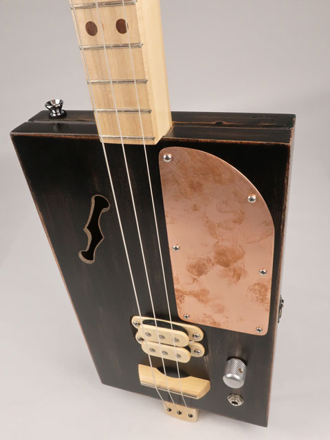 Front view of a 3 string cigar box guitar with a copper pick guard and maple humbucker. This cigar box guitar is handmade by Mike Snowden of Snowden Guitars.