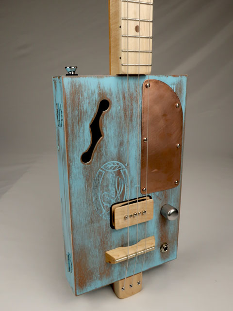Wooden cigar box guitar musical instrument with a blue distressed finish on a gray background made by Mike Snowden.