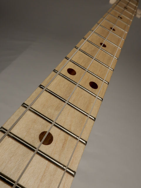 Close-up of a cigar box guitar guitar fretboard with strings on a gray background made by Mike Snowden.