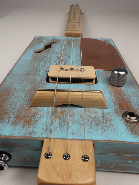 Close-up of a blue cigar box guitar with 3 strings made by mike snowden.
