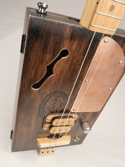 Top angle view of a 3 string cigar box guitar with a copper pick guard and humbucker pickup. Made by Mike Snowden with a Padron cigar box.