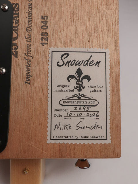 Back view of a cigar box guitar handmade by Mike Snowden of Snowden Guitars. There is a stick on the back of the cigar box guitar with the date and number of guitars made. 