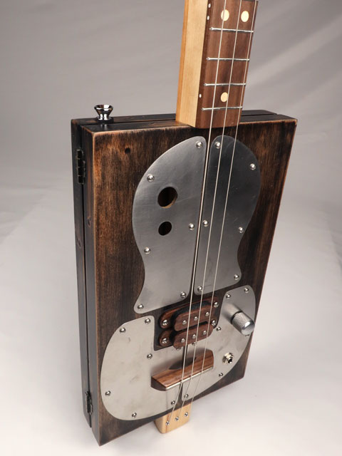 Wooden and metal cigar box guitar with a guitar neck on a gray background made by Mike Snowden.
